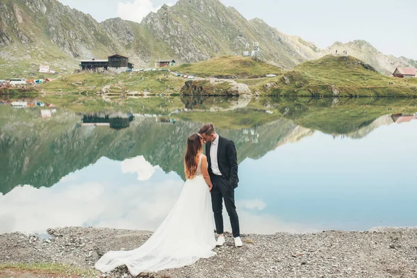 Romantikus házaspár szerelmes áll a háttérben a tó és a hegyi táj. Boldog házaspár. Szerető férfi és nő a házasság napján. — Stock Fotó