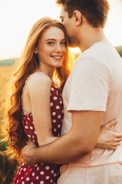 Flickan är glad att känna sig älskad av sin pojkvän, som kramar henne som en hel del tillgivenhet, utanför badade i solljus. Solig dag. Alla hjärtans dag. — Stockfoto