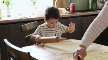 Boy helping grandmother rolling soft dough during pastry preparation in kitchen at home. The intergenerational connection. Different ages together.