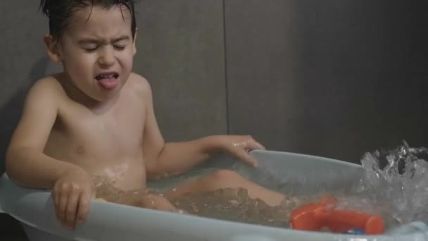Кавказький хлопчик розважається, бризкає воду і посміхається, купаючись у ванній кімнаті. Гігієна у ванній кімнаті. Чудовий портрет для дизайну способу життя. Здорові — стокове відео