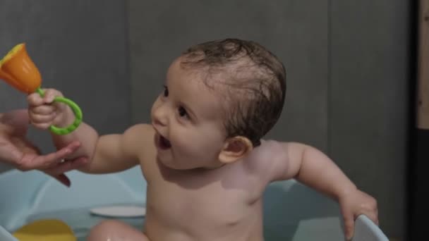Mother washing little girl in a bathtub. Smiling kid in bathroom playing with toy. Mom bathing infant. Parent and kid play with water. — Wideo stockowe