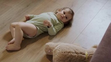 Bebek kız yerde, oyuncak ayısının yanında sırt üstü yatıyor. Kalkıp emeklemeye başlıyor. Bebek bakımı. Aile bakımı.