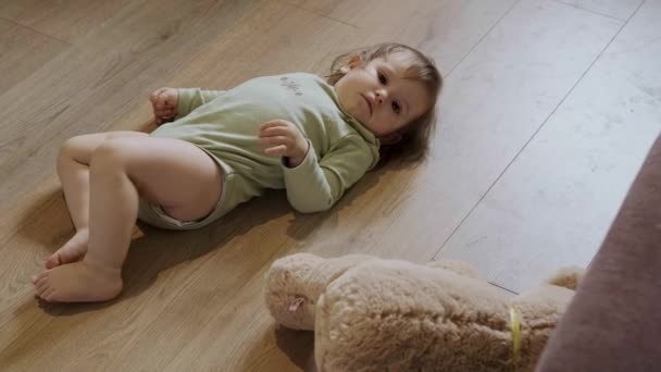 Flickan som ligger på rygg på golvet bredvid sin teddybjörn som stiger upp och börjar krypa. Sköt om dig. Familjeomsorg. — Stockvideo