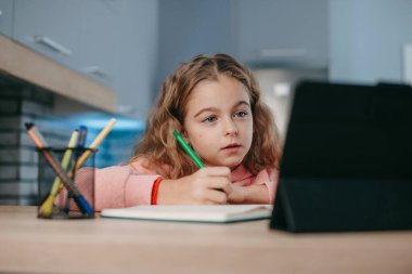 Concentrated girl listening to online lesson looking at tablet screen and taking notes. Online education, remote work. Girl studying online.