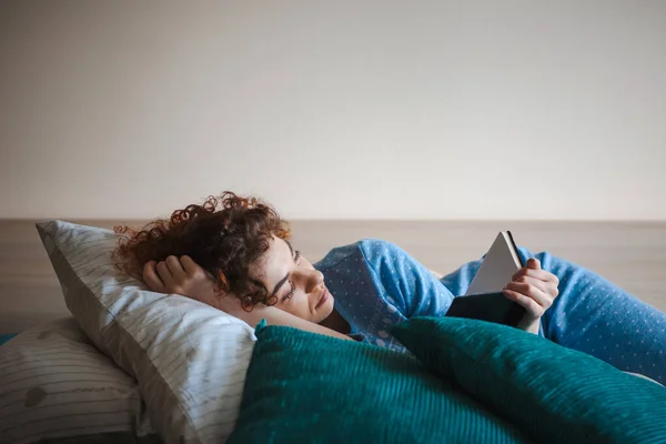 Curly-haired woman hold book novel book at home lying on the couch. Relaxing and enjoying — Foto de Stock