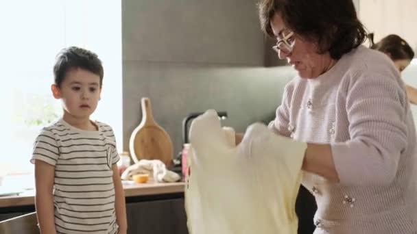 Grandma spinning the dough in the air according to old habits, preparing it for pies. Boy helper looking at his grandmother. Grandmother round dough, great — Stockvideo
