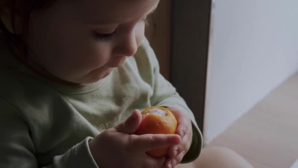 The girl put a whole unpeeled orange in her mouth. Baby care. Holding hands. — Stockvideo