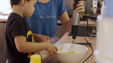 Çocuk, annesinin doğum günü pastası için kremayı elektrikli mikserle karıştırdığı kaseye süt ekliyor. Tatlı yemek. Birlikte yemek pişirmek..