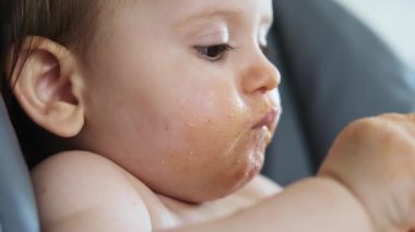 Domates soslu yemek yiyen ve parmak emen bir kızın yakın plan portresi. Bebek dağınık.