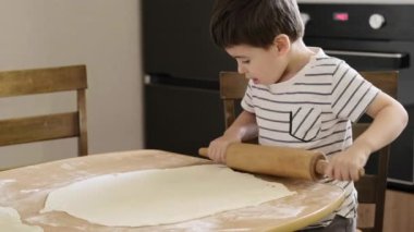 Beyaz çocuk mutfaktaki masanın üzerinde merdaneyle hamur topluyor ve büyükannenin turta pişirmesine yardım ediyor. Hafta sonu sabahı evde..