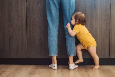 Neşeli bebek yüzünü annesinin ayaklarının arkasına gizliyor. Aile koruması.