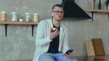 Mutfakta oturmuş elma yerken telefonda konuşan bir adam. İş adamı çalışıyor. Mobil iletişim. Konuşan insanlar. Akıllı telefon tutan insanlar.