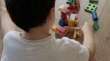 Top view of a boy building tower of block toys sitting on the floor at home. Child development.