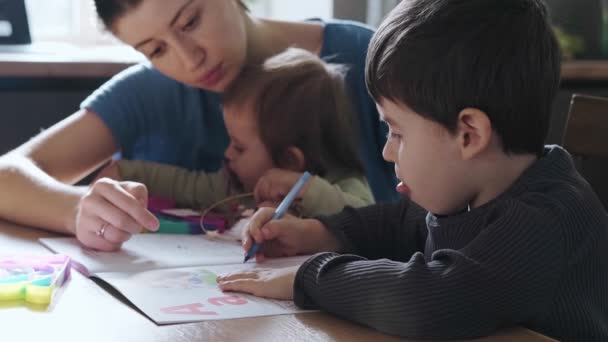 Die Mutter hält das kleine Mädchen in der Hand und bringt ihm bei, seinen Sohn zu schreiben. Bildung, Lernen, Studium. Hausaufgaben. Coronavirus-Schule. — Stockvideo