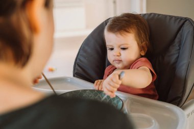 Bir annenin, yüksek sandalyede kaşıkla oturan oğluna bakışı. Anne bebeği besliyor. Mutlu aile birlikte. Sağlıklı yemek..