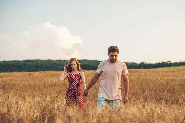 Birbirine aşık bir çift buğday tarlasında romantik vakit geçiriyor. Dışarıda birlikte yürüyen güzel mutlu insanlar. Aile günü. Güneşli bir yaz günü. El ele tutuşarak..