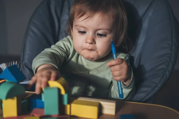 Menina brincando com blocos de construção multicoloridos e segurando uma caneta, sentado em cadeira alta. Desenvolvimento do bebé. De mãos dadas. — Fotografia de Stock