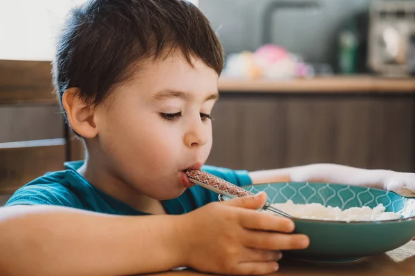 Boy holding a spoonful of rice in his mouth, fooling around at the table. Healthy lifestyle. Healthy food. — Fotografia de Stock