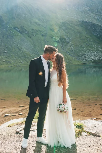 Yeni evli çiftler, göl ve dağ manzarasının önünde öpüşüyorlar. Açık hava manzarası. Güzel yaz manzarası. Doğa manzarası.