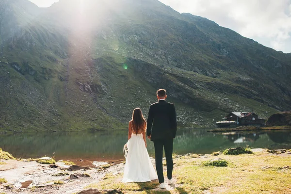 山の中の湖を見て新郎と花嫁のバックビュー ロマンチックな背景 結婚式の旅行 エレガントな結婚式の背景 — ストック写真