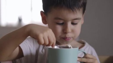Aç küçük çocuk evdeki mutfak masasına yaslanıyor ve fincandan dondurma yiyor. Nefis kahvaltı..