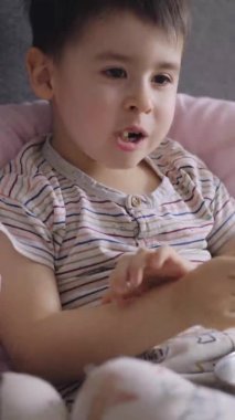 Çocuk TV seyrediyor ve evde patlamış mısır yiyor. Çocuk elinde bir kase patlamış mısır tutuyor..