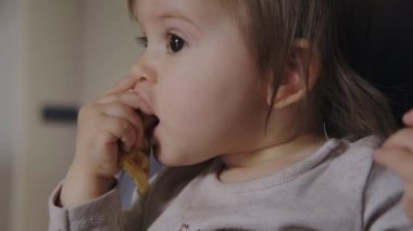 Yüksek sandalyede ekmek yiyen bir kızın yakın plan portresi. Güzel genç kız. Bebek gelişimi. Bebek bakımı.