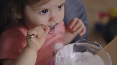 Kaşıkla yemek yiyen mutlu bir kız bebek, kendini besleyen bir bebek, yüksek sandalyede oturuyor, sağlıklı beslenmenin tadını çıkarıyor. İnsanların yaşam tarzı. Gülümseyen mutlu çocuk.