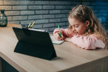 Ödev yapan beyaz bir kızın portresi ve iş yerinde oturup tabletle internetten çalışma. Okula sağ salim dön. Seçici Odaklanma. Görüntülü arama yapılıyor