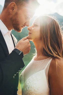 Beyaz gelin ve damadın yan görünüm portresi. Düğün fotoğrafçılığı sırasında gelinlere sarılma ve öpücükler. Yeni evliler dışarıda evleniyor..