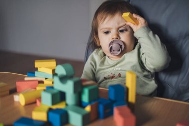Küçük kız evde tahta oyuncaklarla oynuyor. Yüksek sandalyede oturuyor. Bebek gelişimi.