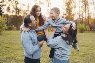 Mutlu aile dışarıda eğleniyor ve gülümsüyor. Ebeveynler parkta çocukları taşır. Aile hafta sonu. Bahar geldi..
