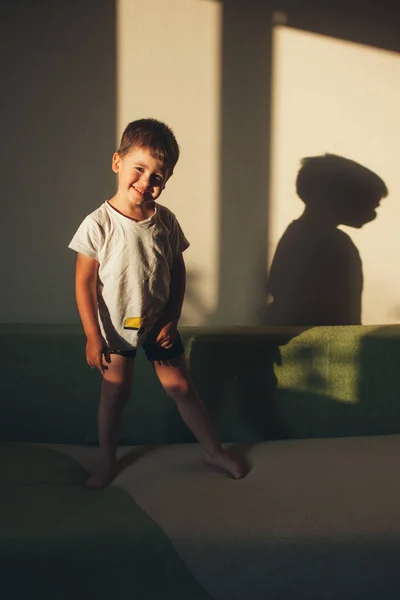 Niño Mirando Cámara Sonriendo Con Cara Linda Pie Sofá Contra —  Fotos de Stock