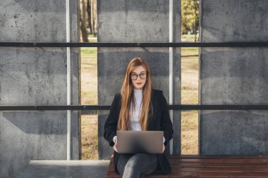Zencefilli iş kadını parktaki bankta otururken bilgisayarını uzaktan kumanda olarak kullanıyor. Eğitim konsepti. Reklamlar. Çevrimiçi eğitim kavramı