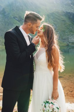 Yazın güneşli bir günde göl kenarında birbirine aşık romantik bir çift. Yeşil arka plan. Açık hava manzarası. Düğün seyahati.