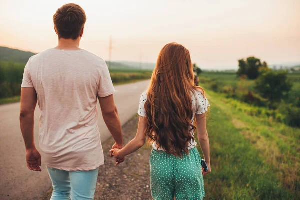 Yolda el ele tutuşan genç bir çiftin arka görüntüsü. Yaz kavramı. Pozitif kişi. Romantik çift çıkıyor..