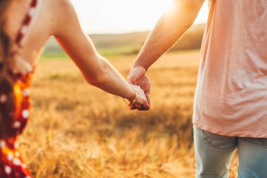 Açık havada buğday tarlasında el ele tutuşan bir çiftin portresini kapatın. Aşkın ve mutlu ilişkinin sembolü. Sevgi dolu bir çift el ele tutuşuyor. Romantizm. Yaz