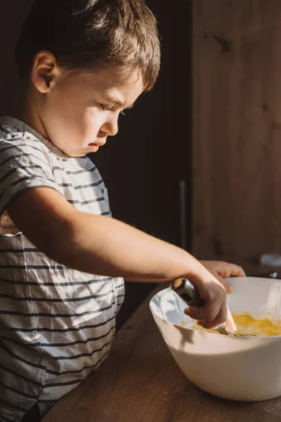 Boy mixing ingredients for a cake in the white bowl. 8 years old child cooking food at home. Child cooking at the kitchen.