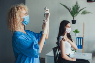 Kadın tıp doktoru şırınga iğnesiyle Covid-19 aşısını çıkarıyor. Hastanede eldiven takıp maske takıyordu. Pandemik önleme. Coronavirüs