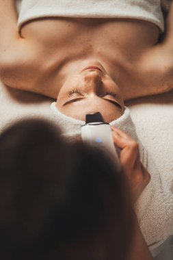 Güzellik uzmanlarının elleri bir kadının yüzüne ultrason temizliği yapıyor. Yüz bakımı. Güzel cilt. Cilt bakımı.