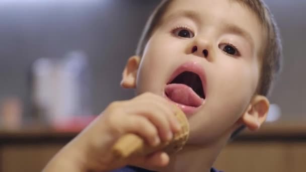 子供が食べる ワッフルコーンでアイスクリームを舐める 屋内で自宅で 興奮した表情をしている — ストック動画
