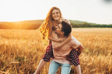 Handsome man giving piggy back ride to his girlfriend at the wheat field. Always happy together.
