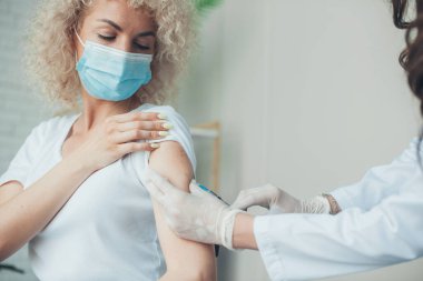 Caucasian curly woman receiving coronavirus vaccine in arm during her appointment in hospital. Vaccination concept. Health care concept. Coronavirus concept.