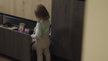 Meraklı küçük kız mutfaktaki çekmecenin içeriğini araştırıyor. Sağlıklı yaşam tarzı tasarımı için. Bebek gelişimi. Sağlıklı bir yaşam tarzı. Bebek bakımı.
