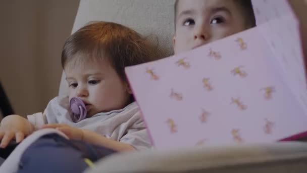 Brother His Baby Sister Reading Book Together Sitting Sofa Living — Stockvideo