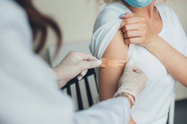 Doctor in rubber protective gloves putting adhesive bandage on patients arm after vaccination. Pandemic prevention. Coronavirus vaccination. Coronavirus