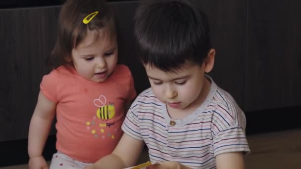 Caucasian Brother Baby Sister Looking Smiling Expression While Reading Magazine — Vídeo de Stock