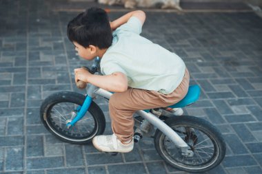 Beyaz çocuk evinin avlusunda bisikletiyle oynuyor. Çocuk özel evde hızlı gidiyor. Çocuk oyunları ve bisiklet sporu.