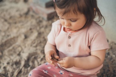 Concentrated baby girl playing in the sand at the playground. Baby development. Outdoor creative activities for kids.