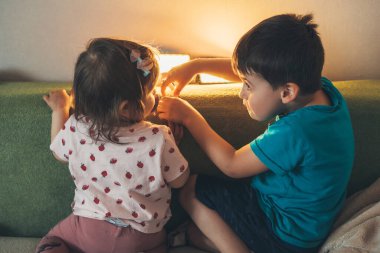 Sevimli erkek ve kız kardeş kanepede birlikte oynarken mutlu hissediyorlar. Mutlu aile tatilleri..